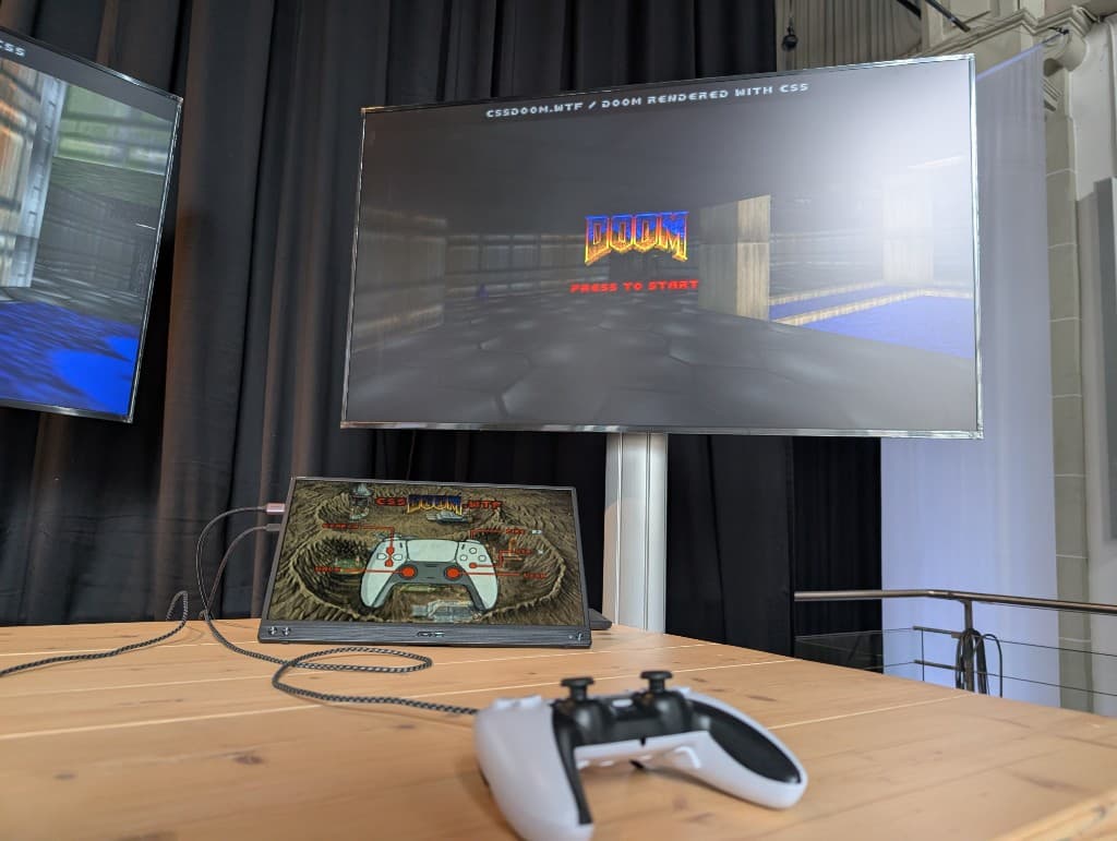 CSS DOOM running on a screen at the CSS Day 2026 conference booth, with a game controller on the table
