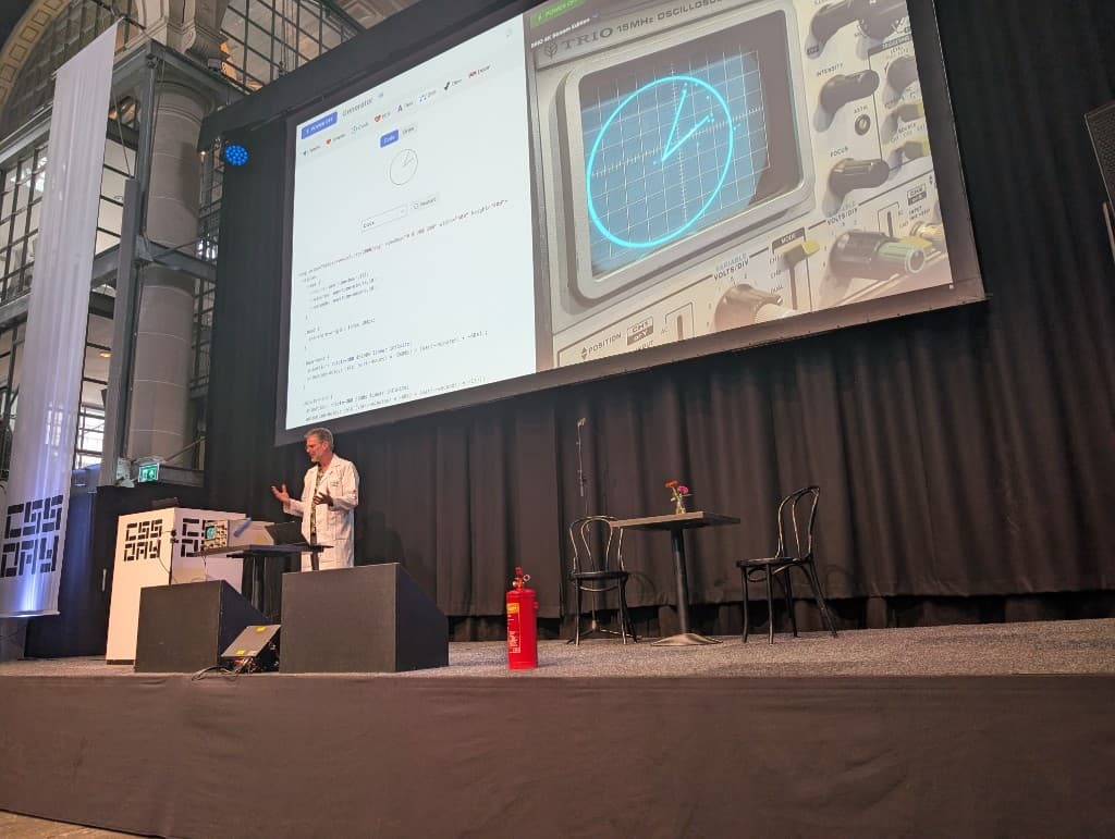 Niels Leenheer on stage at CSS Day 2026 showing an oscilloscope demo on the big screen